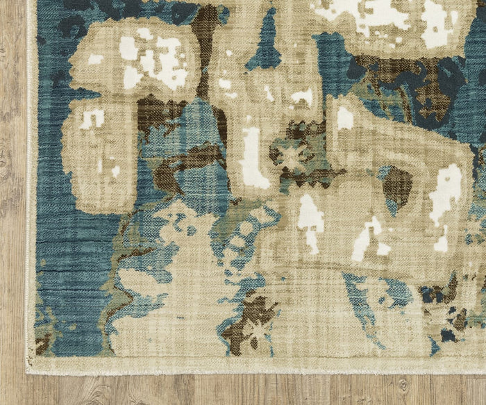 A close-up of the Oriental Weavers Reed / RE11Q Rug reveals its modern abstract design featuring blue, beige, and cream shapes on a wooden floor. The image highlights the rug’s edge and part of the surrounding floor, showcasing the intricate pattern of this power-loomed piece made from space dyed polypropylene.