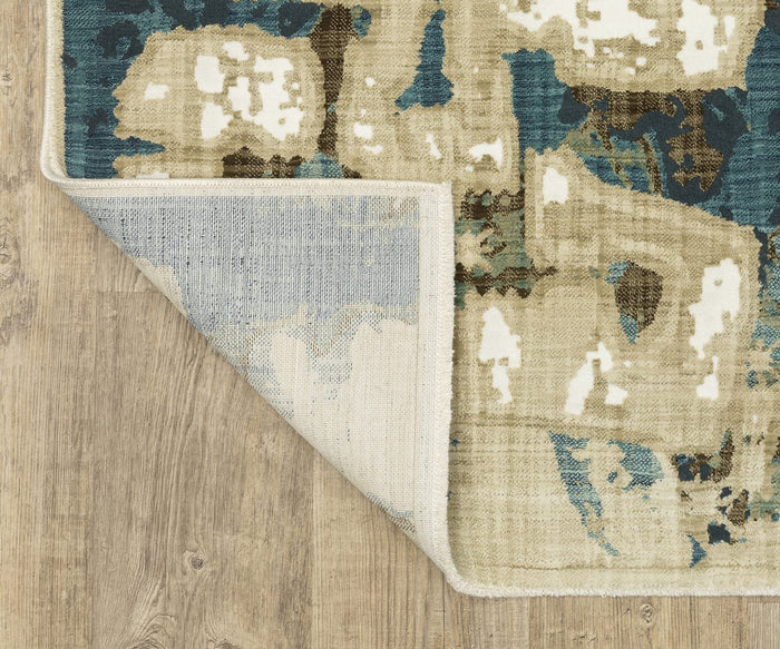 The Oriental Weavers Reed / RE11Q Rug, featuring modern abstract patterns in blue, beige, and white, is displayed on a wooden floor. Power-loomed with space-dyed polypropylene fibers for lasting durability, the rug’s corner is flipped over to reveal its lighter underside and texture.