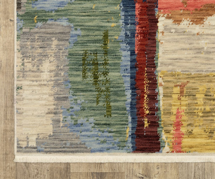 Corner of the Oriental Weavers Soleri / SOL02 Rug showcasing a colorful modern abstract pattern in green, blue, cream, red, yellow, and brown on a wood floor. Expertly crafted as an Axminster rug from a wool-nylon blend, the design is finished with white fringe along the edge for a polished touch.