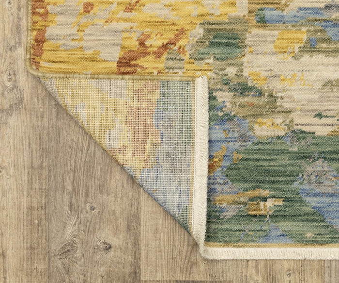 A corner of the Oriental Weavers Soleri / SOL04 Rug from the Soleri Collection is flipped over, showing its underside. This modern abstract area rug, displaying yellow, blue, green, and beige tones, lies atop light wood flooring with distinct grain patterns.