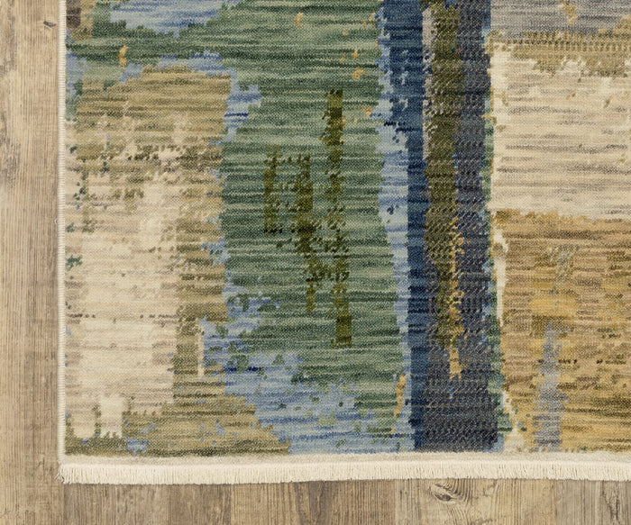 A close-up of the Oriental Weavers Soleri / SOL05 Rug showcases its modern abstract design with textured green, blue, beige, and brown patterns laid over a wooden floor. Fringed edges enhance the rug’s contemporary style with an elegant touch.