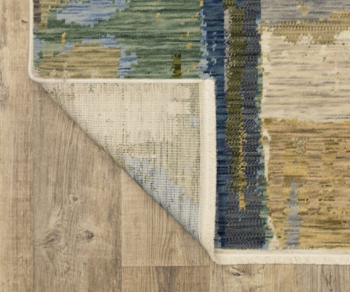 A corner of the Oriental Weavers Soleri / SOL05 Rug is folded over on a light wood floor, revealing the rug’s underside and showcasing a modern abstract Axminster-style pattern in green, blue, beige, and gold tones crafted from a wool and nylon blend.