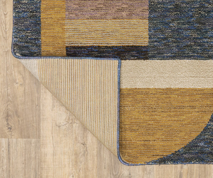The Oriental Weavers Strada / STR01 Rug, showcasing Art Deco-inspired geometric patterns in gold, beige, brown, and blue hues, rests on a light wood floor. One corner of the machine-woven nylon rug is turned over to display its textured underside.