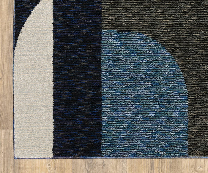 A close-up of the Oriental Weavers Strada / STR03 Rug, a machine-woven nylon piece showcasing geometric shapes in navy, blue, gray, and cream on a light wood floor. The design blends rectangles and semicircles with textured patterns, making this Art Deco rug an ideal accent for modern spaces.