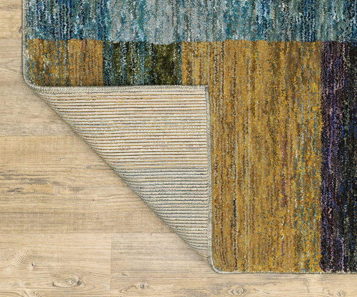 The Oriental Weavers Strada / STR04 Rug, featuring blue, gold, and green tones in a patterned Art Deco design, is partially flipped to reveal its striped backing. Machine-woven from nylon and ideal for modern interiors, it is displayed on a light wood floor.