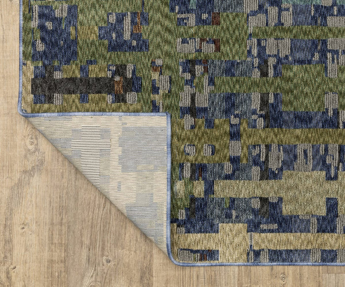 The Oriental Weavers Tisdell / TIS03 Rug, a modern abstract area rug with blue, green, and tan geometric patterns, is shown on a wood floor. Crafted from space-dyed polyester, this durable rug has its bottom left corner turned over to display a lighter, striped underside.