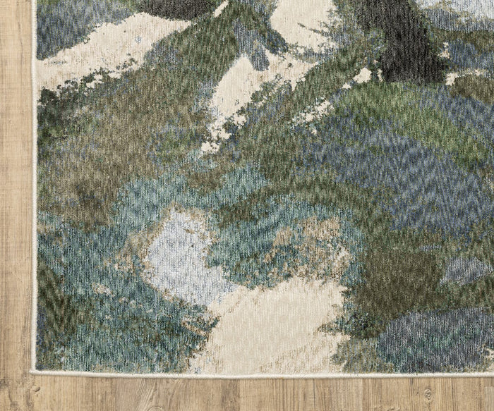 The Oriental Weavers Tisdell / TIS04 Rug featuring blue, green, and cream brushstroke patterns is displayed on a hardwood floor. Showcasing the bold, contemporary design typical of modern abstract rugs, this piece adds dynamic flair to any space. The edges of the rug are visible along the left and bottom sides of the image.