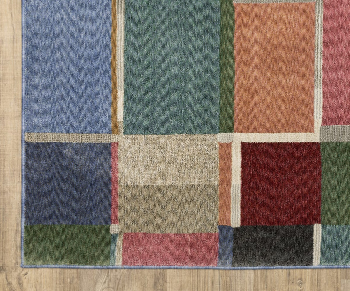 A close-up of the Oriental Weavers Tisdell / TIS05 Rug, a rectangular space-dyed polyester area rug featuring a patchwork pattern of blue, green, beige, red, pink, and orange squares on a light wooden floor. This durable rug infuses any room with vibrant color and contemporary style.