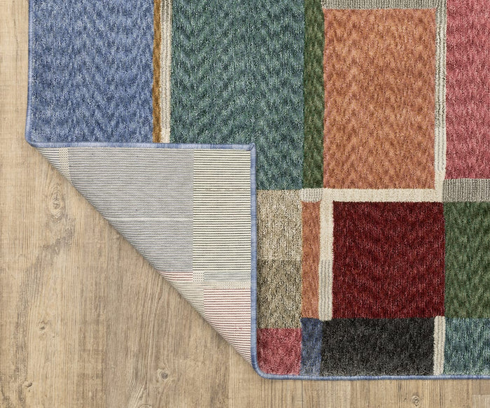 The Oriental Weavers Tisdell / TIS05 Rug, crafted from space-dyed polyester, displays a vibrant patchwork design on a wood floor, with one corner flipped up to reveal its striped underside. This durable area rug combines striking color with resilience to enhance any room.