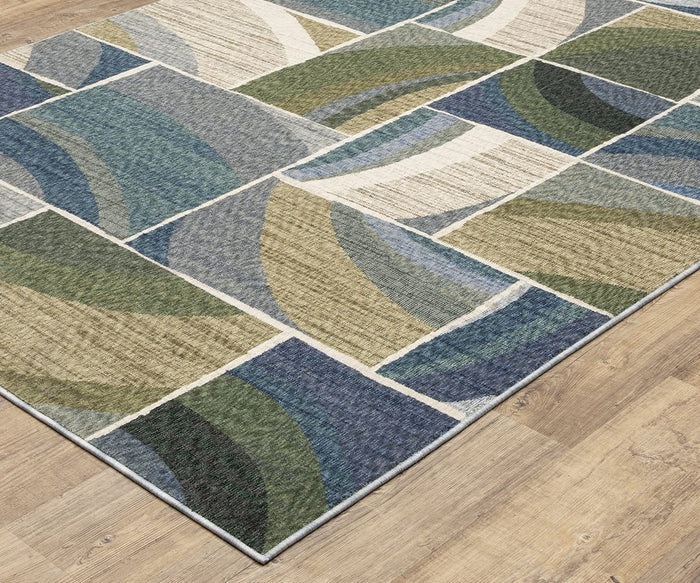 The Oriental Weavers Tisdell / TIS06 Rug, crafted from space-dyed polyester, showcases an abstract pattern with curved shapes in blue, green, beige, and gray tones. This durable area rug is displayed on a light wood floor.
