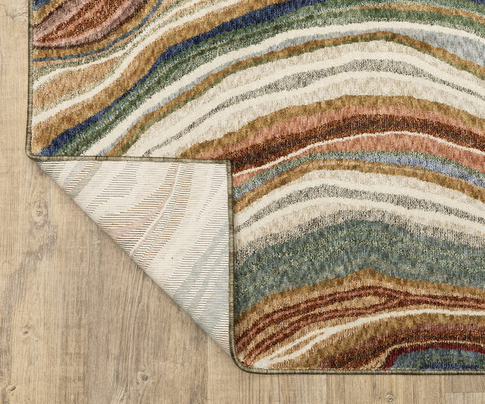 The Oriental Weavers Tisdell / TIS07 Rug, featuring wavy, layered patterns in earth tones and vibrant space-dyed polyester, lies on a light wood floor. One corner is flipped over to reveal its light striped underside, showcasing the rug’s modern abstract style and durable construction.