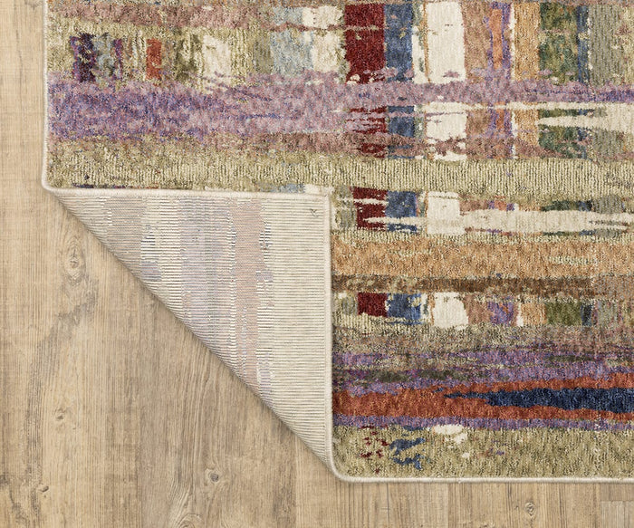 A close-up of the Oriental Weavers Tisdell / TIS08 Rug showcases its vibrant, abstract pattern set atop a wooden floor. One corner of this modern rug is flipped over, revealing both the contrasting backing design and the underside.