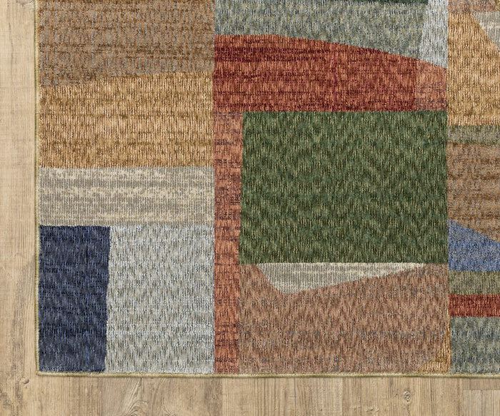 A close-up of the Oriental Weavers Tisdell / TIS09 Rug, featuring a space-dyed polyester design with multicolored geometric shapes in green, red, beige, blue, and brown on a light wood floor. The rug displays a textured woven pattern.