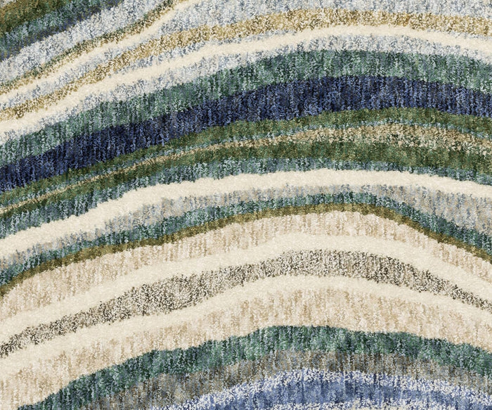 Experience the contemporary style of the Oriental Weavers Tisdell / TIS10 Rug, featuring a close-up of its wavy, layered stripes in shades of blue, green, beige, white, and gray for a natural, textured look. Crafted from space-dyed polyester for durability and lasting quality, this area rug seamlessly combines modern design with practical elegance.
