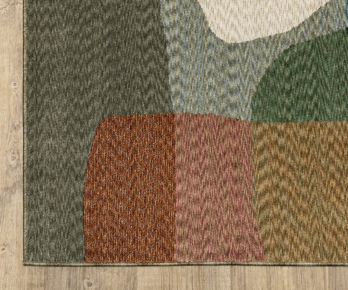 A corner of the Oriental Weavers Tisdell / TIS11 Rug, featuring an abstract pattern in green, red, gold, white, and blue space-dyed polyester, is placed on a light wooden floor.