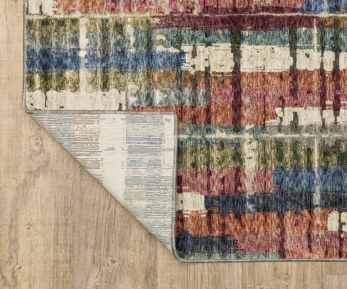The Oriental Weavers Tisdell / TIS12 Rug, displayed on a wooden floor, showcases multicolored abstract and textured patterns. One corner is flipped over to reveal the rug’s lighter, striped underside. Crafted with space-dyed polyester, this modern rug offers enhanced durability and vibrant color variation.