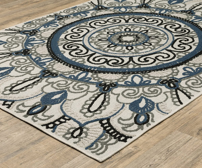 The Oriental Weavers Torrey / 072J1 Rug is a rectangular piece from the Torrey Collection, featuring intricate circular and floral patterns in blue, black, and gray with abstract motifs on a beige background in neutral tones, displayed here on a light wood floor.