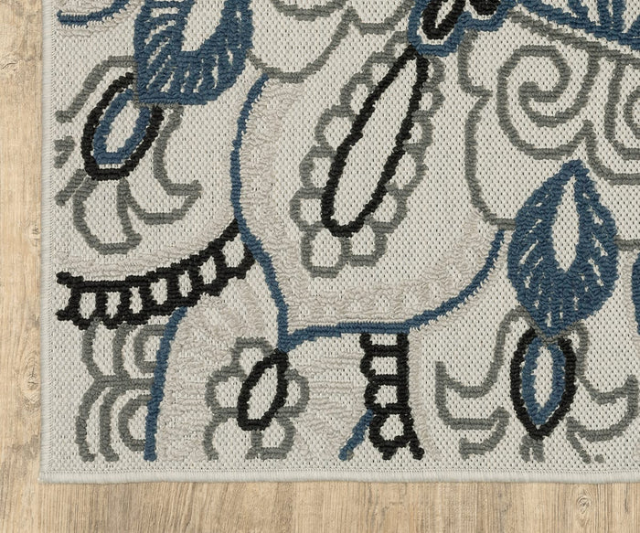 A close-up of the Oriental Weavers Torrey / 072J1 Rug featuring blue, black, and gray abstract floral and leaf patterns on a beige background, highlighting its modern motifs and neutral tones, displayed on a light wood floor.