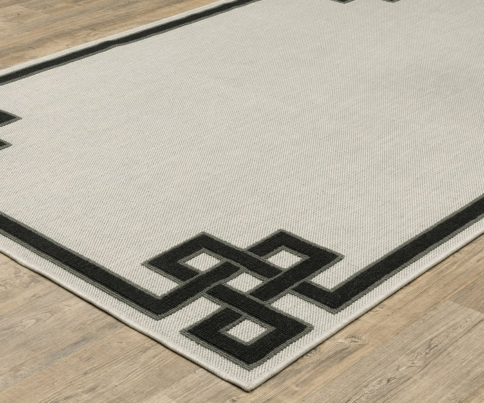 The Oriental Weavers Torrey / 1530I Rug features a beige center with a black geometric border of interlocking square designs, adding dynamic texture to your space. Shown here on a light wood floor, this rug is part of the Torrey Collection.