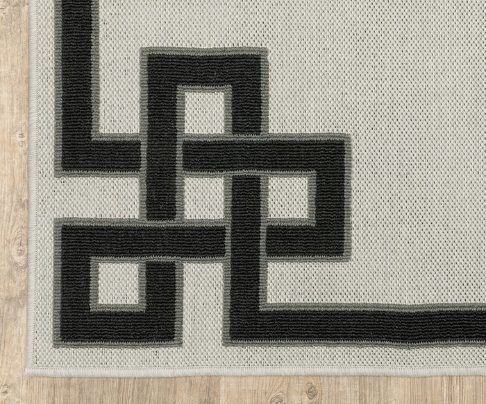 Corner of the Oriental Weavers Torrey / 1530I Rug, showcasing its textured light gray surface with a bold black geometric border featuring interlocking square patterns and dynamic texture, placed on a light wood floor.