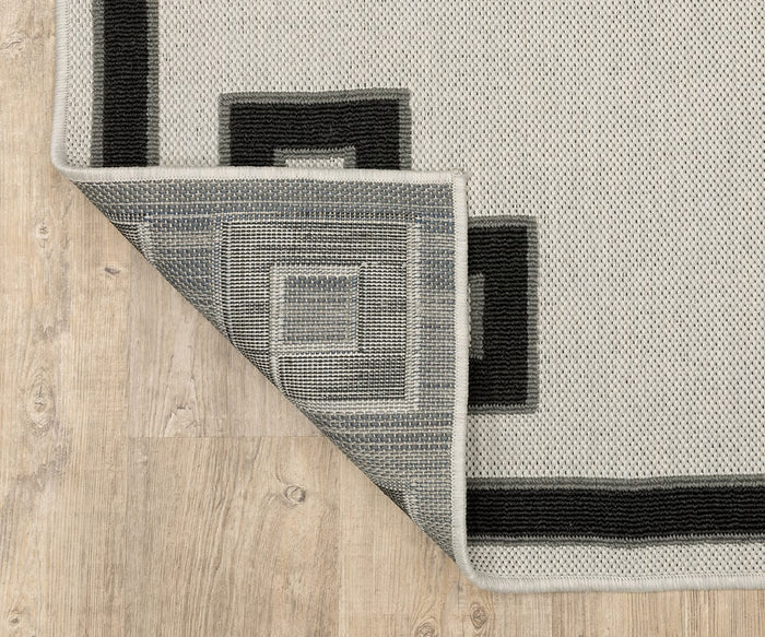 An Oriental Weavers Torrey / 1530I Rug in beige and black geometric patterns from the Torrey Collection rests on a light wood floor, its dynamic texture accentuated by one folded corner that reveals the reverse side, which features similar abstract motifs in muted tones.