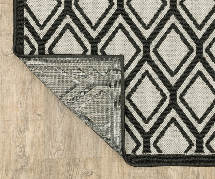 The Oriental Weavers Torrey / 4151G Rug, featuring a black and white diamond pattern, is partially flipped over to reveal its underside. Part of the Torrey Collection, this area rug rests on a light wood floor, with its neutral tones and subtle abstract motifs adding modern elegance to any space.