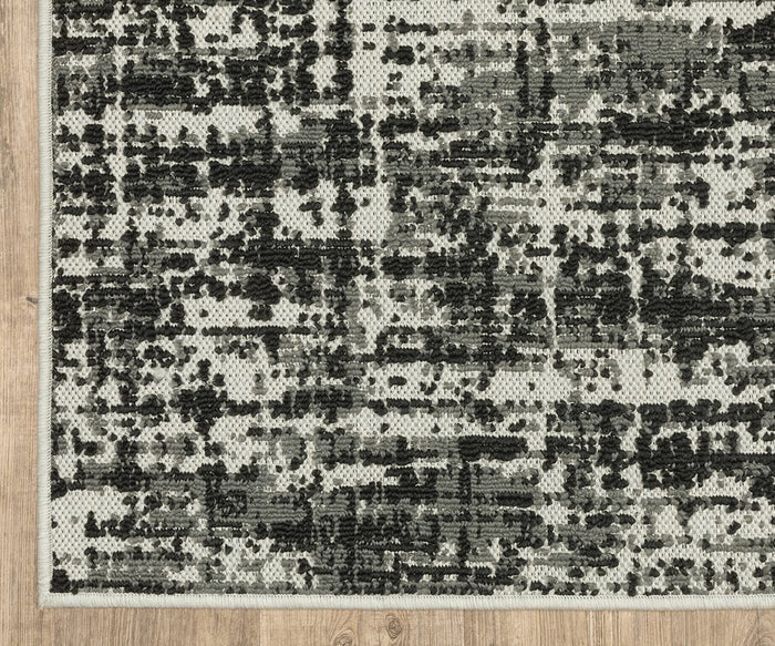 A close-up of the Oriental Weavers Torrey / 531W Rug shows its modern flatwoven design with black and gray abstract motifs on a light background, placed on a wooden floor.