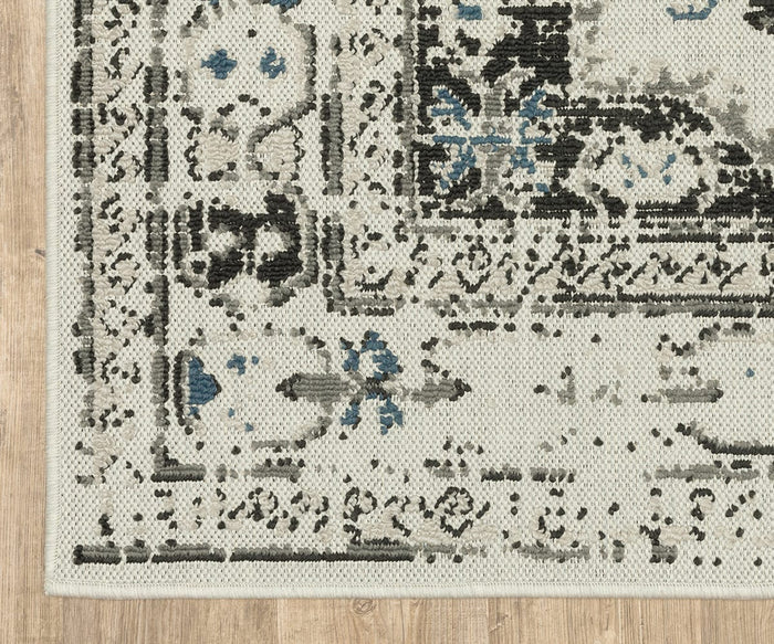 A close-up of the Oriental Weavers Torrey / 5561H Rug highlights its cream, black, and blue abstract motifs and decorative border, showcased atop a wooden floor. The rug features a layered texture and intricate patterns from the Torrey Collection.