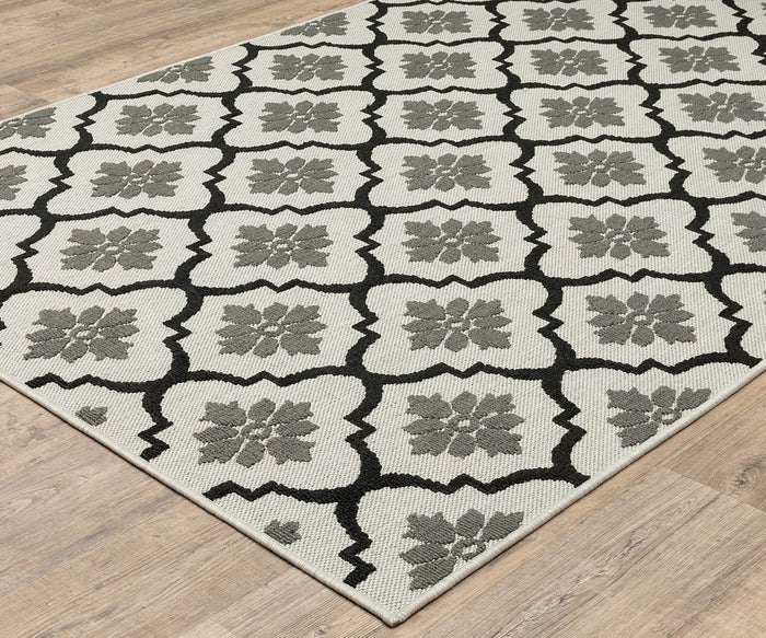 The Oriental Weavers Torrey / 5562E Rug, a beige flatwoven rug with a repeating geometric floral pattern in gray and black and dynamic texture, is placed on a light wood floor.