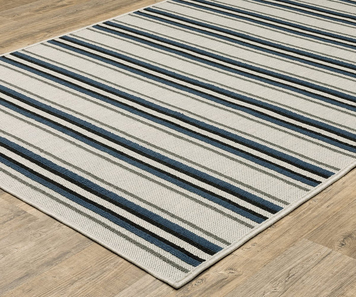 An Oriental Weavers Torrey / 5571Y Rug rests on a wood floor, showcasing horizontal stripes in shades of blue, gray, black, and white. Subtle abstract motifs add visual interest, while the dynamic texture enhances both the appearance and feel of this modern accent piece.