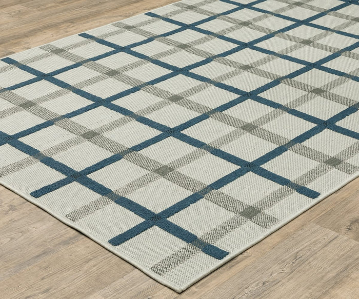 The Oriental Weavers Torrey / 7150H Rug, a rectangular flatwoven piece with a cream background and a plaid pattern of intersecting blue and gray lines that beautifully blends neutral tones, is shown placed on a light wood floor.