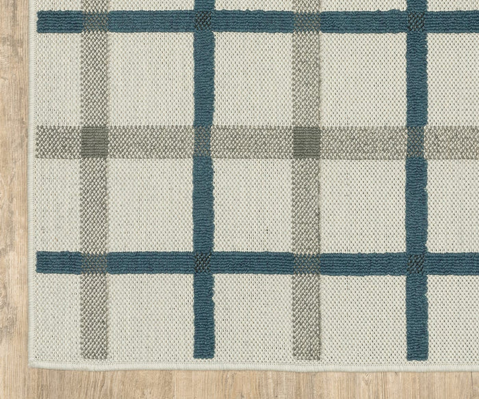 The Oriental Weavers Torrey / 7150H Rug, a flatwoven design in beige featuring a grid pattern of blue and gray lines, lies on a light wood floor. The edges of the rug are visible along the left and bottom sides of the image, introducing subtle neutral tones to the space.