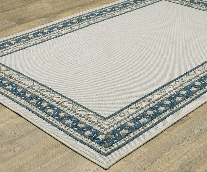 The Oriental Weavers Torrey / 8020W Rug, a rectangular area rug from the Torrey Collection, displays a light beige center with decorative blue and gray border patterns featuring abstract motifs, adding dynamic texture to a light wood floor.
