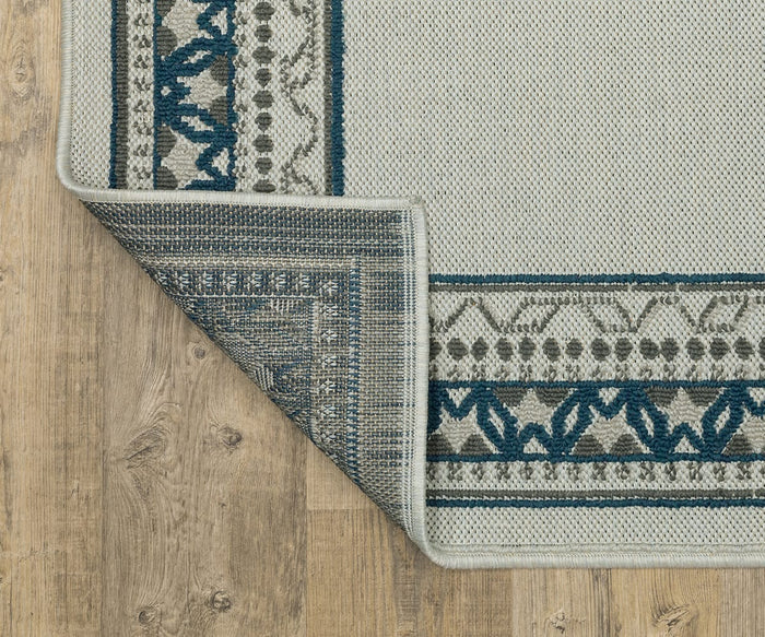 A corner of the Oriental Weavers Torrey / 8020W Rug, showcasing blue and gray patterns, is folded over to reveal the backing. The rug features dynamic texture and is placed on a light wooden floor.