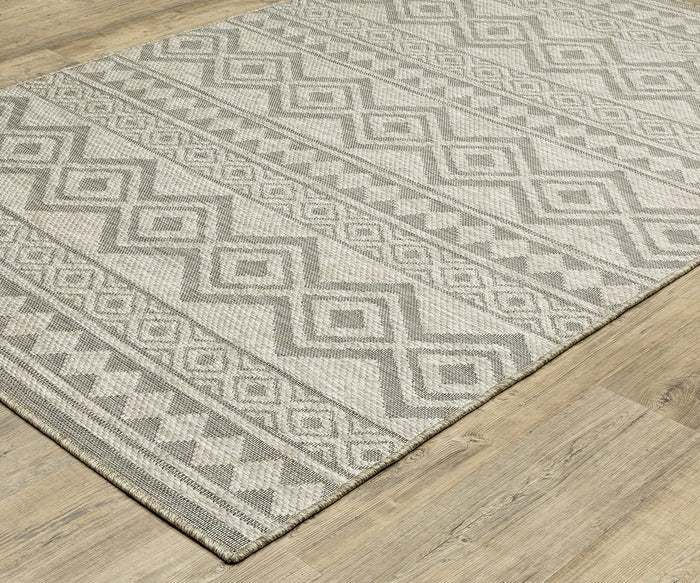 The Oriental Weavers Tortuga / TR03A Rug, in beige and gray with geometric diamond and zigzag patterns, rests on a light wood floor. Crafted from durable polypropylene, this area rug from the Tortuga Collection combines easy-care practicality with stylish design—perfect for any living space.