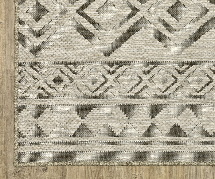 The Oriental Weavers Tortuga / TR03A Rug, in beige and gray, showcases geometric patterns of diamonds, zigzags, and lines as it rests on a light wood floor. Crafted from easy-care polypropylene, this rug blends modern style with everyday practicality for any contemporary living space.
