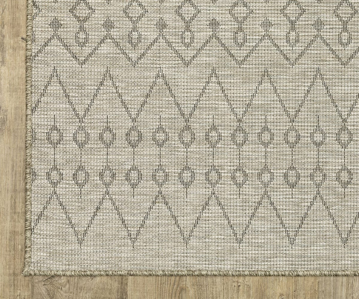 The Oriental Weavers Tortuga / TR04A Rug, featuring a beige woven base with a black geometric diamond and dot pattern, lies on a light wood floor. Its slightly fringed edge and symmetrical, repetitive design make it an easy-care rug ideal for everyday living.
