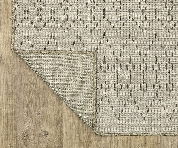 The Oriental Weavers Tortuga / TR04A Rug, featuring a beige background with a globally inspired geometric black pattern, is displayed on a wooden floor. One corner is folded over to showcase the texture and underside of this easy-care rug.