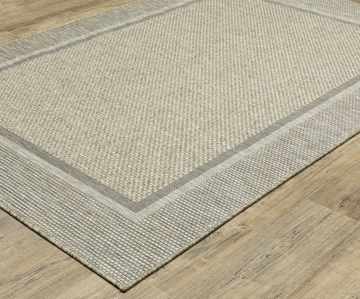 A rectangular beige and gray Oriental Weavers Tortuga / TR06A Rug, featuring a textured pattern and solid border in easy-care polypropylene, is placed on a light wood floor.