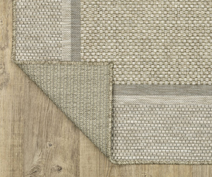 A close-up of the Oriental Weavers Tortuga / TR06A Rug in beige, featuring a woven texture with one large corner folded back to reveal its darker, textured underside. This easy-care rug is displayed on light-colored wood-look flooring.