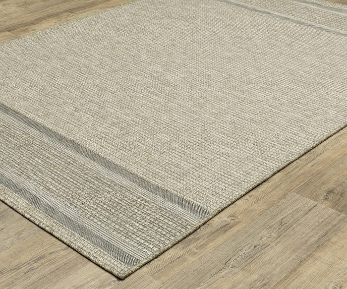 The Oriental Weavers Tortuga / TR07A Rug, a beige woven area rug from the Tortuga Collection with subtle gray stripes at the edges, sits on a light wood floor. This easy-care rug features a textured, grid-like pattern and boasts a neutral, minimalist look.