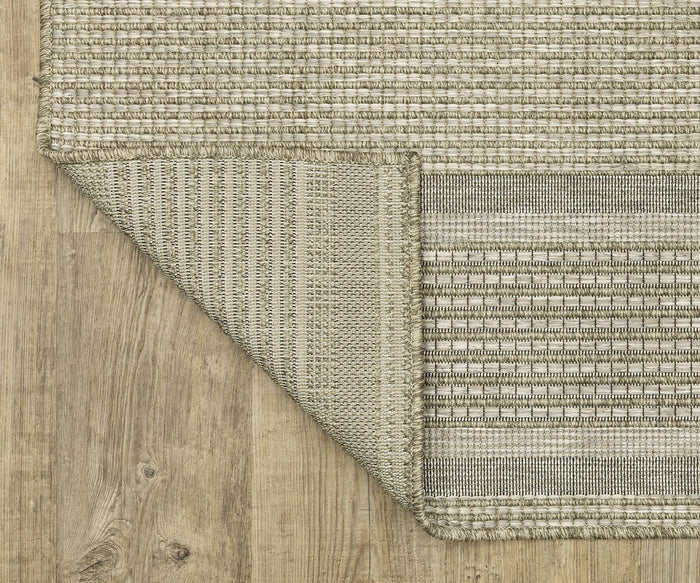 The Oriental Weavers Tortuga / TR07A Rug, shown here in beige with a stylish striped design and one corner folded to display the underside, is crafted from easy-care polypropylene and displayed on a light wood floor.