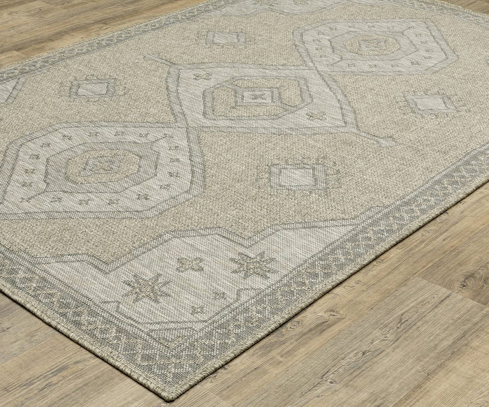 The Oriental Weavers Tortuga / TR08A Rug, featuring beige and gray geometric patterns with octagonal shapes and decorative borders, is placed on a wood floor. This stylish area rug from the Tortuga Collection combines easy-care practicality with elegant design accents.