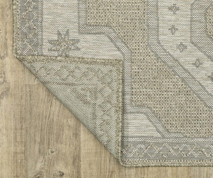 The Oriental Weavers Tortuga / TR08A Rug, featuring a beige and light brown pattern, is shown with one corner flipped to display the underside. This easy-care polypropylene rug from the Tortuga Collection is placed on a light wood floor.