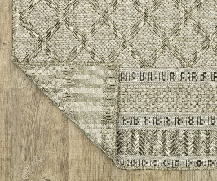 An Oriental Weavers Tortuga / TR10A Rug in beige, featuring a diamond pattern and power-loomed construction, is displayed on a wood floor with one corner flipped over to show the contrasting design on the reverse side.