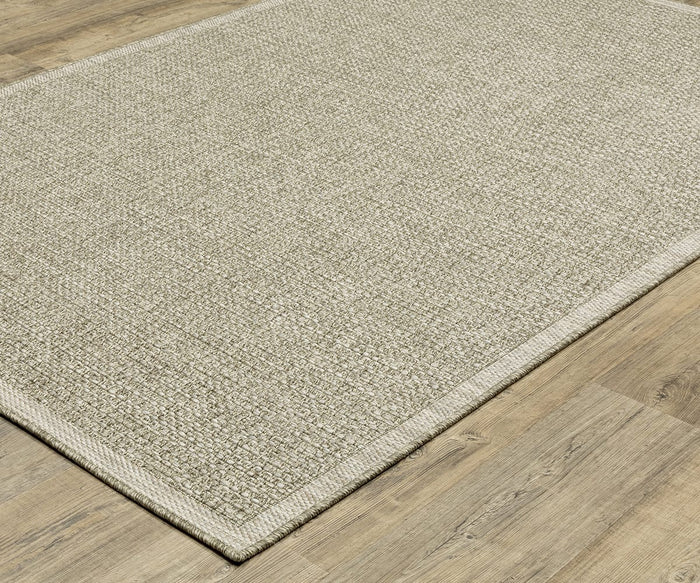 An Oriental Weavers Tortuga / TR12A Rug, featuring a beige textured design and a simple border, is displayed on a light wood floor. Crafted from easy-care, power-loomed polypropylene, the rug is photographed from above at an angle to highlight its surface and part of the surrounding floor.