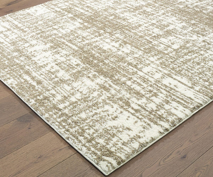 A corner of the Oriental Weavers Verona / 1803J Rug, featuring a beige and cream distressed abstract pattern, is shown on a medium brown wood floor. Only part of this neutral palette rug is visible.