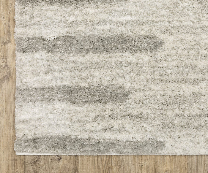 A close-up of the rectangular Oriental Weavers Verona / 5605HG Rug, featuring a textured surface in shades of gray and white, placed on a light brown wooden floor. This polyester microfiber rug showcases a neutral palette that effortlessly complements modern interiors.