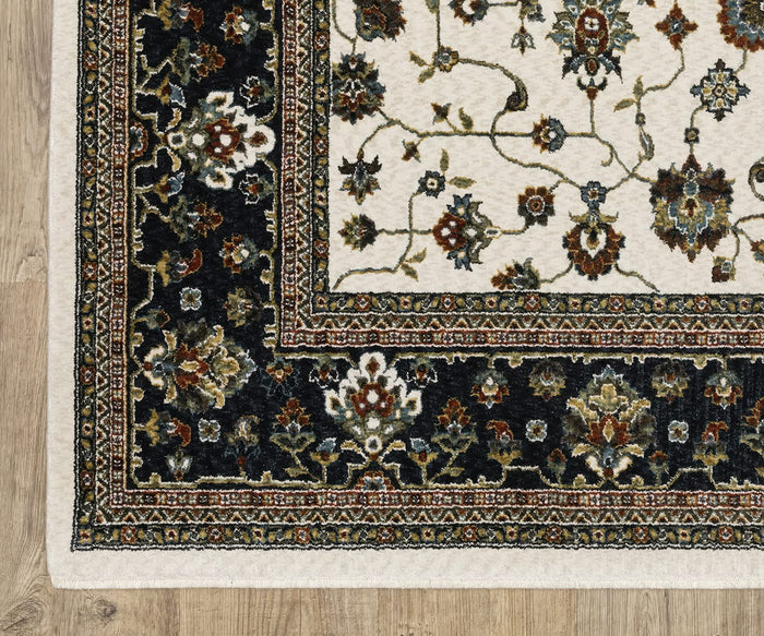 A close-up of the Oriental Weavers Vivian / VI02B Rug placed on a wooden floor. This rectangular rug, crafted from microfiber polyester, features Persian-inspired ornate floral patterns with a dark border and lighter inner area, detailed colorful designs, and ivory edging.