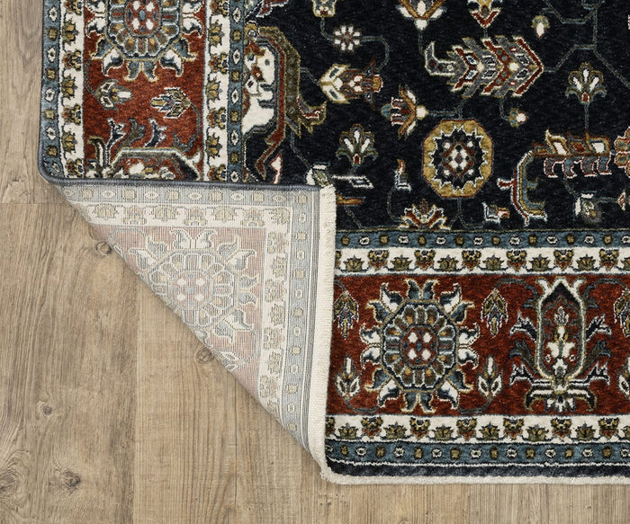 A corner of the Oriental Weavers Vivian / VI05A Rug is folded over on a wooden floor, highlighting its ornate floral patterns on the surface and a more muted version on the back. This Persian-inspired rug showcases a traditional color palette of red, black, ivory, and blue.